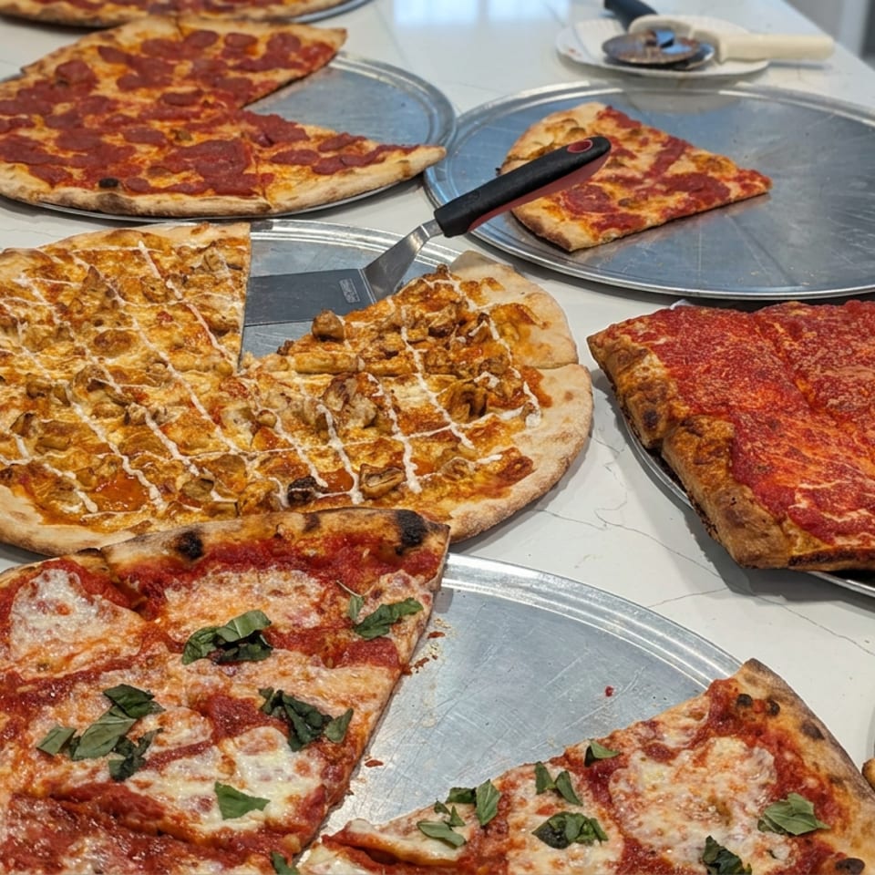 Assorted round and rectangular pizzas with pepperoni, cheese, mushrooms, and basil displayed on metal serving trays.