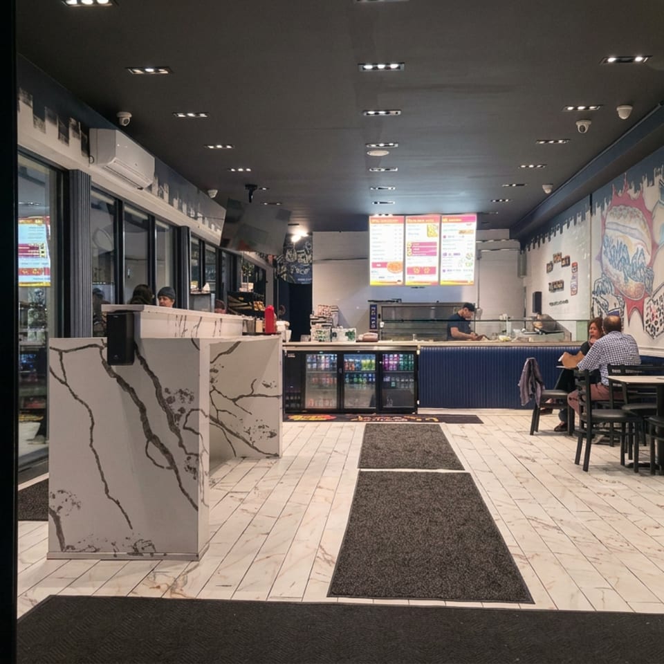 Modern casual restaurant interior with mural-covered walls, illuminated menu screens, counter service, beverage coolers, and seated diners.